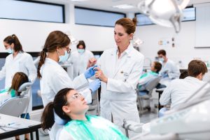 Estudiantes con bata blanca realizando prácticas de odontología en una clínica universitaria en España.